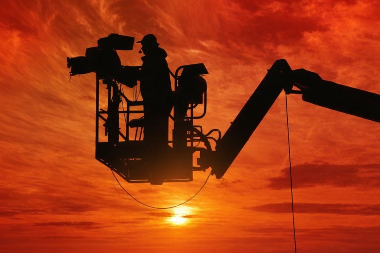 Kameramann in einer Hebebühne bei Sonnenuntergang, vor rotem Himmel